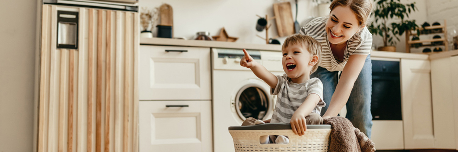 Parent pushing  a child across a kitchen in a basket