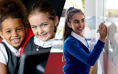 Primary children smiling and secondary school girl writing on white board